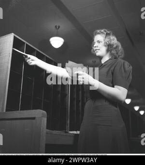 Eine Frau in einem Büro im Jahr 1942. Eine junge Mitarbeiterin steht mit einem Bündel von Notizen in der Hand und sortiert sie in verschiedene Fächer auf einem Regal vor ihr. 1942 Kristoffersson Ref. B135-1 Stockfoto