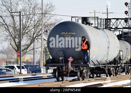 Franklin Park, Illinois, USA. Ein Schaltmann fährt auf dem Bahnsteig und hält die Schiene eines beladenen Tankwagens auf dem letzten Wagen eines Güterzuges. Stockfoto