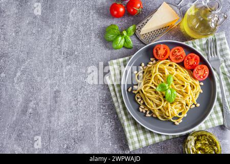 Pasta-Pesto, Spaghetti mit Pesto-Sauce und frischen Basilikumblättern in schwarzer Platte auf grauem Steinhintergrund mit Kopierraum, serviert mit Zutaten. Stockfoto