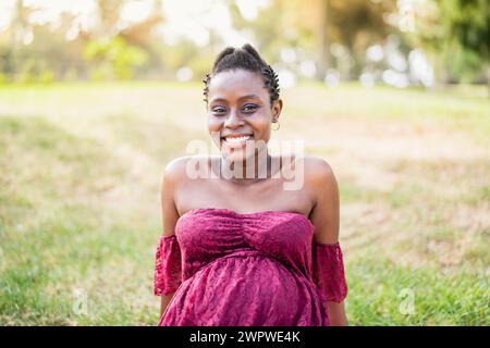 Glückliche afrikanische schwangere Frau lächelt vor der Kamera in einem öffentlichen Park - Maternity Lifestyle Concept Stockfoto