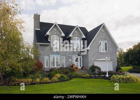 Zeitgenössisches zweistöckiges Haus mit grauen Ziegelsteinen und weißem Ziegel mit halloween-Dekorationen und landschaftlich gestaltetem Vorhof im Herbst. Stockfoto