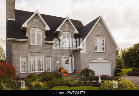 Zeitgenössisches zweistöckiges Haus mit grauen Ziegelsteinen und weißem Ziegel mit halloween-Dekorationen und landschaftlich gestaltetem Vorhof im Herbst. Stockfoto