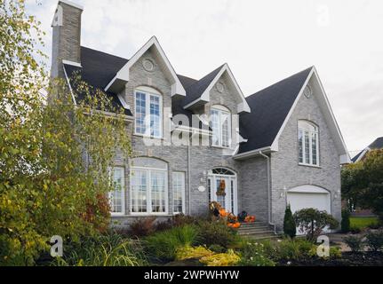 Zeitgenössisches zweistöckiges Haus mit grauen Ziegelsteinen und weißem Ziegel mit halloween-Dekorationen und landschaftlich gestaltetem Vorhof im Herbst. Stockfoto