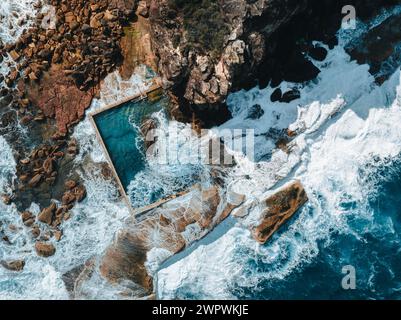 Luftaufnahme am frühen Morgen mit Meereswellen, die während des Sturms über Felsen um den North Curl Ocean Rock Pool fließen. Stockfoto