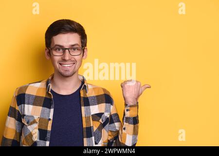Nahaufnahme Porträt eines hübschen jungen Mannes, der mit Daumen auf den Kopierraum für Werbung zeigt, Produkt, Verkauf, Rabatt, Geschäft, offene Stelle. Isoliert auf gelber Wand. Werbung, Werbekonzept Stockfoto