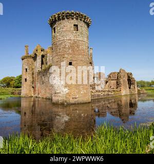 Die Ruinen der Burg spiegeln sich im umgebenden Graben an einem klaren, sonnigen Tag in Südschottland wieder. Stockfoto