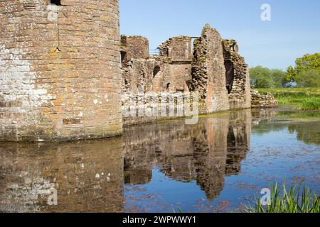 Die Ruinen der Burg spiegeln sich im umgebenden Graben an einem klaren, sonnigen Tag in Südschottland wieder. Stockfoto