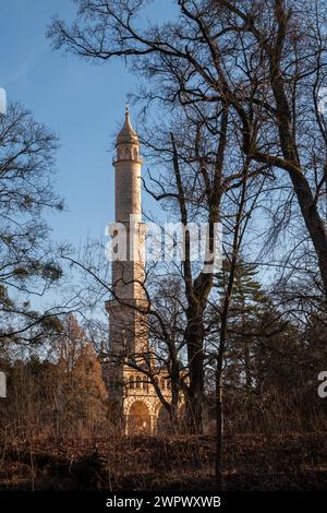 Blick von der Seite des Flusses Dyje auf ein hohes Minarett - Aussichtsturm im Park. Im Spätwinter von vielen blattlosen Bäumen umgeben. Hellblaues SK Stockfoto