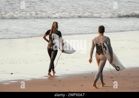 Nicht erkennbare Surfer gehen am Strand in Neoprenanzügen und halten ihre Surfbretter Stockfoto