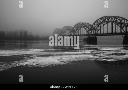 Rigaer Eisenbahnbrücke über den nebligen Daugava Fluss schwarz-weiß 28.02.2024 Stockfoto