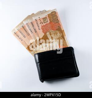 5000 5000 Rupien Banknoten, die mit einer schwarzen Ledergeldbörse ausgerichtet sind. Pakistan State Bank offizielle Geldscheine 2024 isoliert auf weißem Hintergrund. Stockfoto