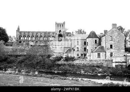 Schwarz-weiß-Blick auf Jedburg am Fluss Jedwater, mit den majestätischen Ruinen der Abteikirche Jedburg im Hintergrund Stockfoto