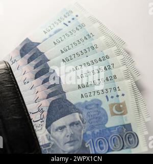 1000 Rupien Banknoten, die mit einer schwarzen Ledergeldbörse verbunden sind. Pakistan State Bank offizielle Geldscheine 2024 isoliert auf weißem Hintergrund. Stockfoto