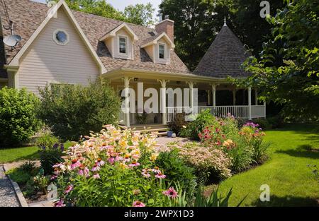 Zweistöckiges beige und braune Landhaus mit Pavillon und lila Echinacea purpurea - Coneflower, gelbe Hemerocallis - Taglilien, rote Monardas in der Grenze. Stockfoto