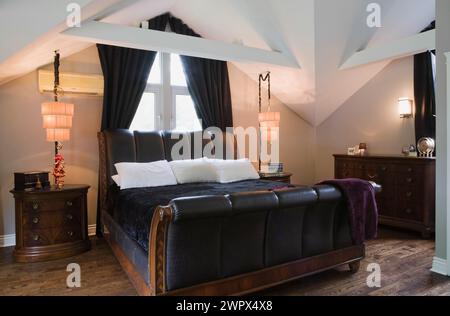 Schwarzes Leder und brauner Holzrahmen King-Size Schlittenbett im Hauptschlafzimmer mit Hartholzboden im luxuriösen Haus. Stockfoto