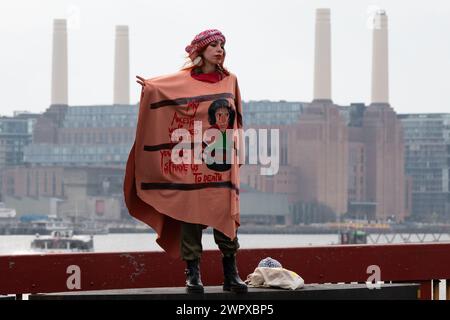 London, Großbritannien. März 2024. Eine Frau mit traditionellem palästinensischem Kopfschmuck und verziertem Schal steht auf der Vauxhall-Brücke, mit dem Kraftwerk Battersea im Hintergrund, während Zehntausende palästinensischer Unterstützer zur US-Botschaft marschieren, um einen Waffenstillstand und ein Ende der britischen und US-Unterstützung für die Belagerung Israels zu fordern. Bombardierung und Invasion des Gazastreifens. Quelle: Ron Fassbender/Alamy Live News Stockfoto