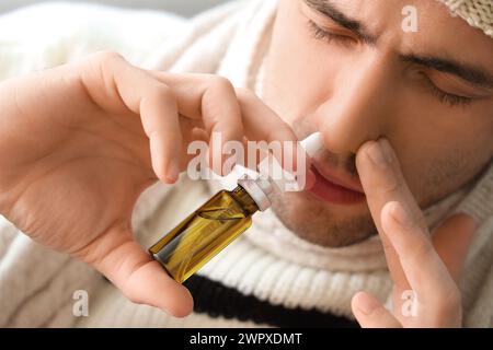 Kranker junger Mann, der zu Hause Nasentropfen benutzt, Nahaufnahme Stockfoto