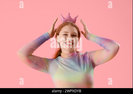 Lächelnde junge Rothaarige Frau in Krone auf rosa Hintergrund Stockfoto