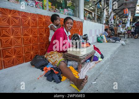 Toliara, Madagaskar – 1. Mai 2019: Unbekannte ältere Madagassische Frau sitzt auf der Straße neben dem Markt, Kind auf dem Rücken, repariert Kleidung mit h Stockfoto