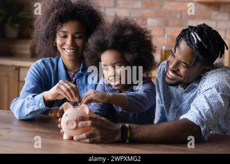 Afrikanisches Paar mit einer kleinen Tochter, die Münzen in die Schweinebank legt Stockfoto