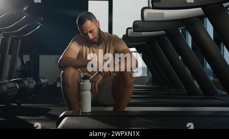 Müder afroamerikanischer Mann sitzen auf dem Laufband entspannen nach einem harten körperlichen Workout Cardio Training in Fitness Club Gym erschöpfter schweißtreibender Sportler Läufer Stockfoto