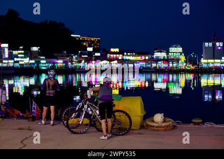 Sokcho City, Südkorea - 30. Juli 2019: Zwei Radfahrer ruhen sich aus und genießen den Blick über das ruhige Wasser des Daepo Port bei Nacht, mit der Atmosphäre Long Stockfoto