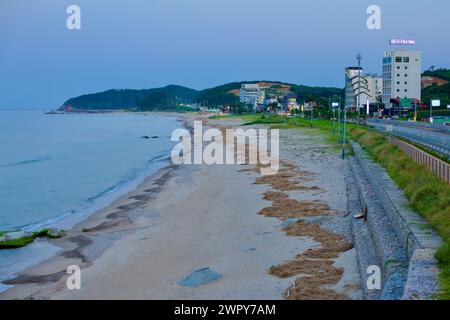 Yangyang County, Südkorea - 30. Juli 2019: Ein Blick nach Süden auf Jeongam Beach bei Einbruch der Nacht, mit Hotels und Motels entlang der Straße Stockfoto