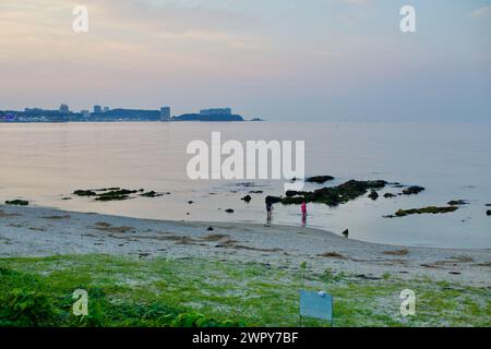 Yangyang County, Südkorea - 30. Juli 2019: Ein eindrucksvoller Blick auf den Jeongam Beach nach Sonnenuntergang, mit zwei Besuchern, die in der Nähe von Felsen im flachen Wasser wateten Stockfoto