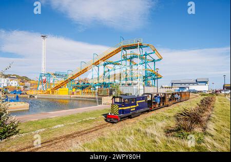 Hastings Miniatur-Eisenbahnlok „Speedy Fizzle“ vor der drehenden Pinball X-Achterbahn im Flamingo Park, Old Hastings, East Sussex, England Stockfoto