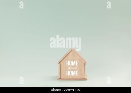 Vereinfachtes hölzernes Hausmodell isoliert auf blassgrünem Hintergrund, mit Text Home Sweet Home on Wall Stockfoto