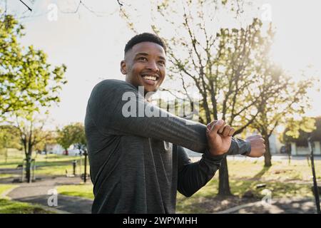 Junger schwarzer Mann in Sportkleidung lächelt beim Stretching im Park Stockfoto