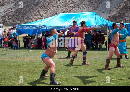 CHOVD, MONGOLEI - 6. JULI 2017: Mongolisches Nomadenlager. Mongolische Wrestler, die in der Natur kämpfen. Zuschauer in Nationalkleidung beobachten den Wettbewerb. Stockfoto