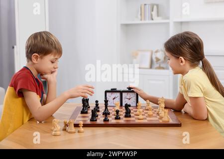 Niedliche Kinder, die Schach am Tisch im Zimmer spielen Stockfoto