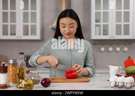 Kochprozess. Schöne Frau, die Paprika auf der weißen Arbeitsplatte in der Küche schneidet Stockfoto