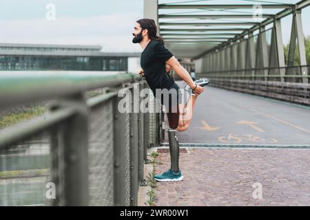 Adaptiver Sportler mit Beinprothesenaufwärmung auf einer Brücke - Schwerpunkt auf Bestimmung und adaptivem Sport. Stockfoto