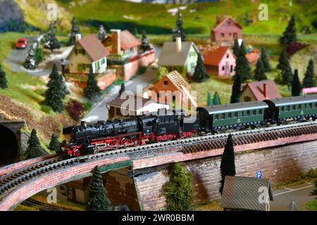 Miniaturbahnmodell mit Modelldampflokomotivzug in Bergambiente. Spielzeugzug Stockfoto