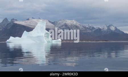 Großer Eisberg Grönland Nanortalik schwimmt im ruhigen arktischen Meeresfjord mit reflektierenden schneebedeckten Bergen im Hintergrund Stockfoto