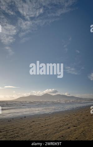 Trübe Mourne Berge in der Nähe des Tyrella Strandes; Strand und Meer im Vordergrund; sonniger Morgen; blauer Himmel und hohe weiße Wolken. Stockfoto