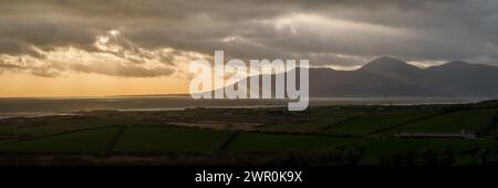 Blick über die Dundrum Bay zu den Bergen Newcastle und Mourne, mit Ackerland im Vordergrund; dunkler Winternachmittag; Sonnenstrahlen durch Wolken; Briefkastenformat. Stockfoto