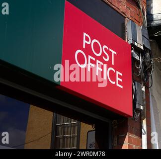 Post Office-Logo einer Ladenfront in Faringdon, Oxfordshire, England mit einem Teil des alten Rathauses in der Fensterspiegelung Stockfoto