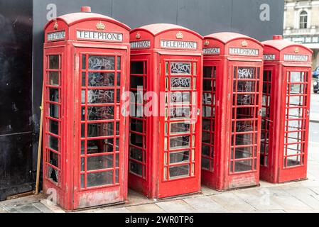 Reihe von vandalisierten ikonischen roten Telefondosen in London, Großbritannien. Vier alte Telefonboxen mit kaputten Fenstern und Graffiti Stockfoto