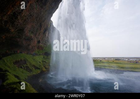 Seljalandsfoss, ein berühmter und einzigartiger Wasserfall in Island mit Besuchern, die hinter den Wasserfällen in eine kleine Höhle laufen. Trip-Konzept. Stockfoto