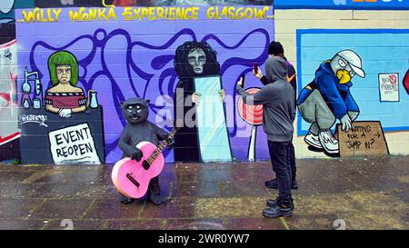 Glasgow, Schottland, Großbritannien. 10. März 2024: Willy’s Chocolate Experience Conceptual Picture als Fans zu den Kunstwerken am Ufer des Flusses clyde abstiegen. Willy Wonka Debacle Wandgemälde erschien auf der clyde Side Graffiti Wand auf dem clyde Walkway. Das Gemälde wurde von dem Künstler Ejek geschaffen, nachdem das Film Experience Event zu nationalen Nachrichten wurde. Das Kunstwerk zeigt die Schauspielerinnen, die bei der Veranstaltung als Oompa Loompa und „The Unknown“ aus dem Skript für künstliche Intelligenz arbeiteten. Credit Gerard Ferry/Alamy Live News Stockfoto