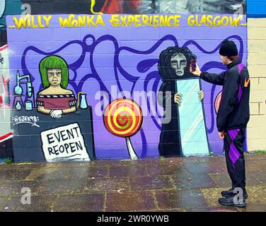 Glasgow, Schottland, Großbritannien. 10. März 2024: Willy’s Chocolate Experience Fan Kai und sein Freund stiegen zu den Kunstwerken am Ufer des Flusses clyde ab. Willy Wonka Debacle Wandgemälde erschien auf der clyde Side Graffiti Wand auf dem clyde Walkway. Das Gemälde wurde von dem Künstler Ejek geschaffen, nachdem das Film Experience Event zu nationalen Nachrichten wurde. Das Kunstwerk zeigt die Schauspielerinnen, die bei der Veranstaltung als Oompa Loompa und „The Unknown“ aus dem Skript für künstliche Intelligenz arbeiteten. Credit Gerard Ferry/Alamy Live News Stockfoto