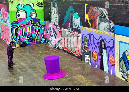 Glasgow, Schottland, Großbritannien. 10. März 2024: Willy’s Chocolate Experience Conceptual Picture als Fans zu den Kunstwerken am Ufer des Flusses clyde abstiegen. Willy Wonka Debacle Wandgemälde erschien auf der clyde Side Graffiti Wand auf dem clyde Walkway. Das Gemälde wurde von dem Künstler Ejek geschaffen, nachdem das Film Experience Event zu nationalen Nachrichten wurde. Das Kunstwerk zeigt die Schauspielerinnen, die bei der Veranstaltung als Oompa Loompa und „The Unknown“ aus dem Skript für künstliche Intelligenz arbeiteten. Credit Gerard Ferry/Alamy Live News Stockfoto