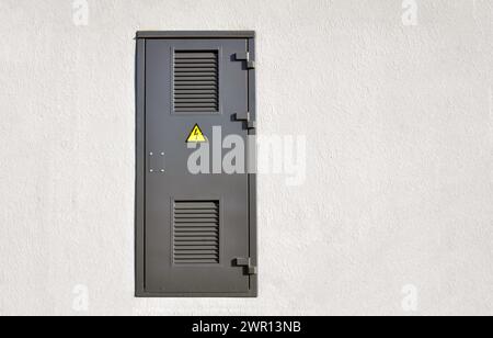 Graue Metalltür gegen eine weiße Wand. Elektrische Gefahr. Stockfoto