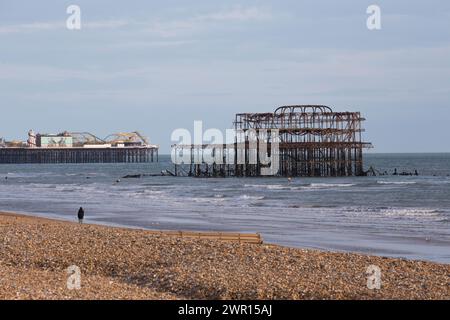 Zwei Piers am Brighton Beach UK mit einer Einzelperson am Strand Stockfoto