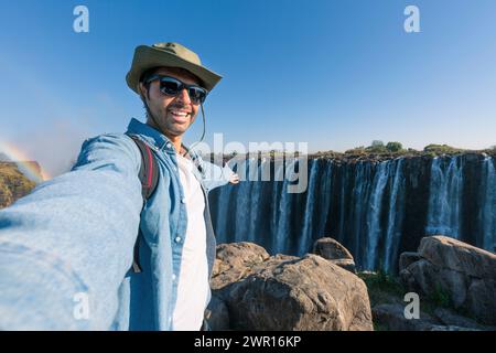 Ein Tourist macht ein Selfie an den Victoria Falls am Sambesi River, der an der Grenze zwischen Sambia und Simbabwe liegt, dem größten Wasserfall der Welt Stockfoto