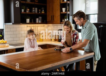 Eine herzerwärmende Szene entfaltet sich, während eine Familie einen köstlichen Schokoladenkuchen zusammen in der Wärme ihrer sonnendurchfluteten Küche genießt und Lächeln und cr teilt Stockfoto