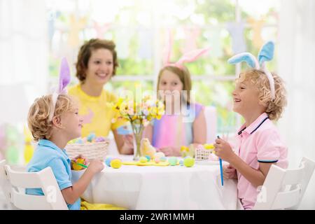 Mutter und Kinder färben Ostereier. Mama, kleines Mädchen und Junge mit Hasen Ohren sterben und malen für Ostereiersuche in weißen sonnigen Zimmer. Stockfoto